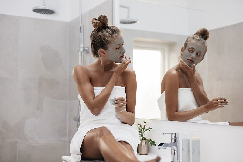 Woman applying a beauty mask and looking at the mirror inside a bathroom
