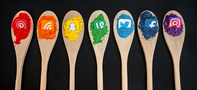 Different Social media logos placed on woden spoons with colored sand on each spoon