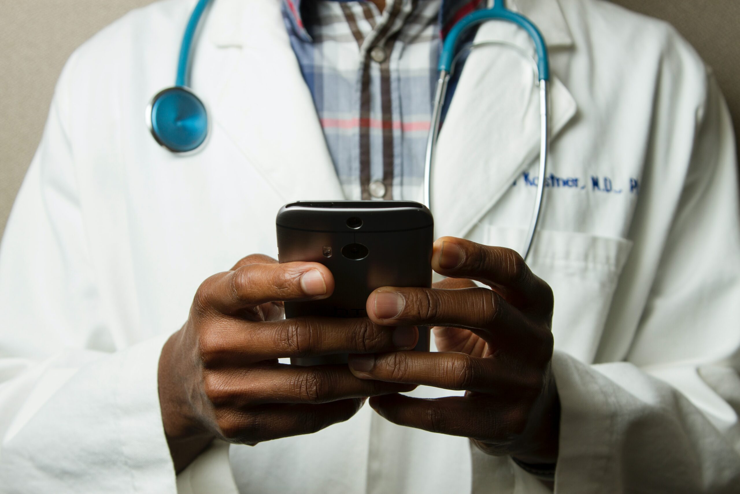 Person typing on his phone and wearing a white coat and a stethoscope
