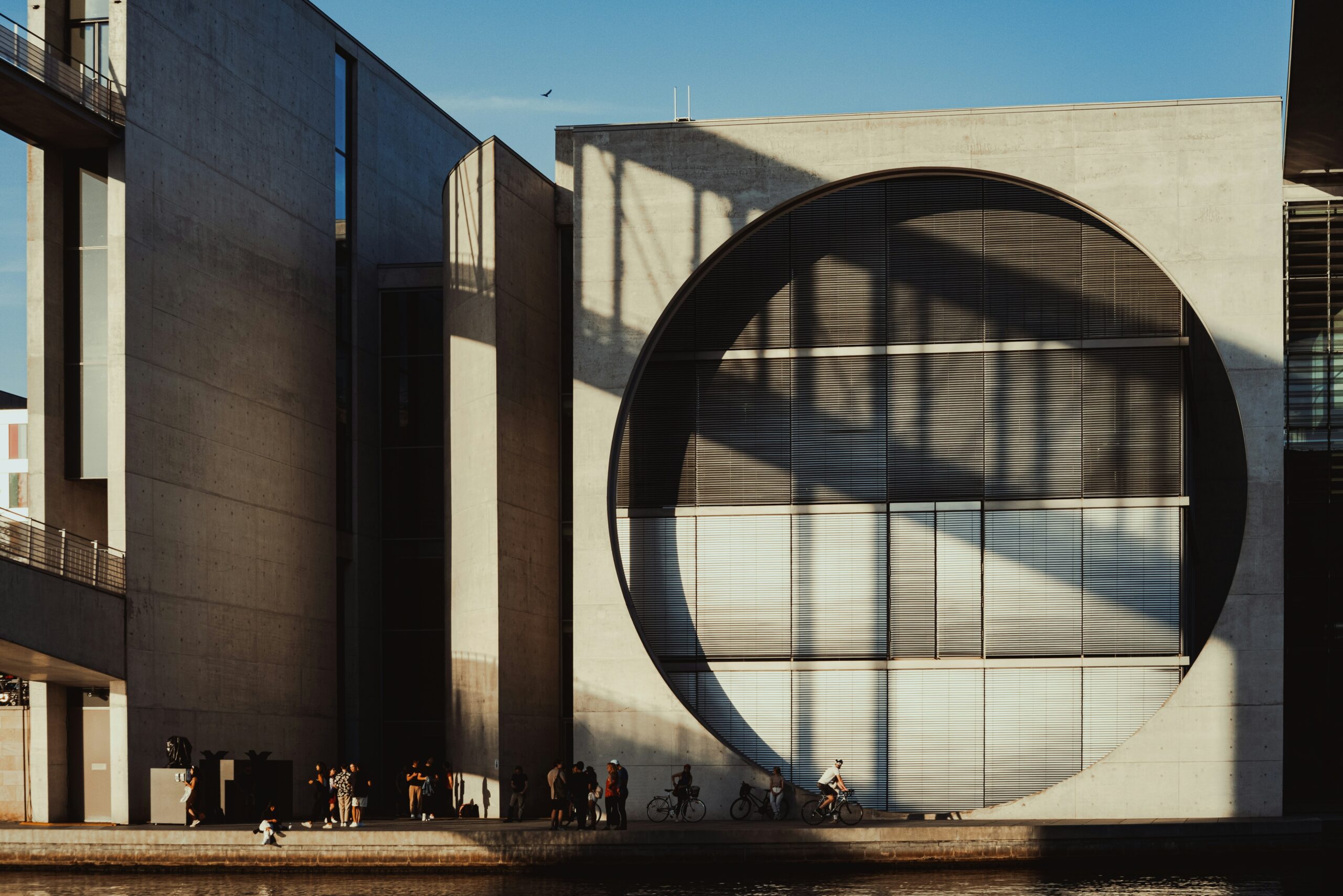 A group of people standing outside of a building next to a body of water